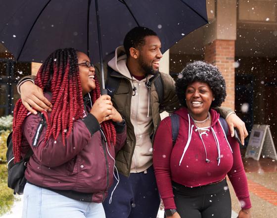 Three students with an umbrella walking in the snow